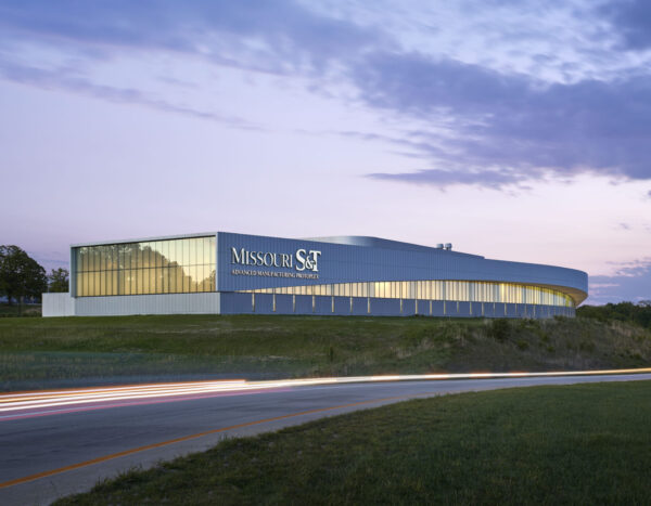 Exterior of the Missouri Protoplex at Missouri S&T at dusk, showing the curved illuminated façade and campus approach.